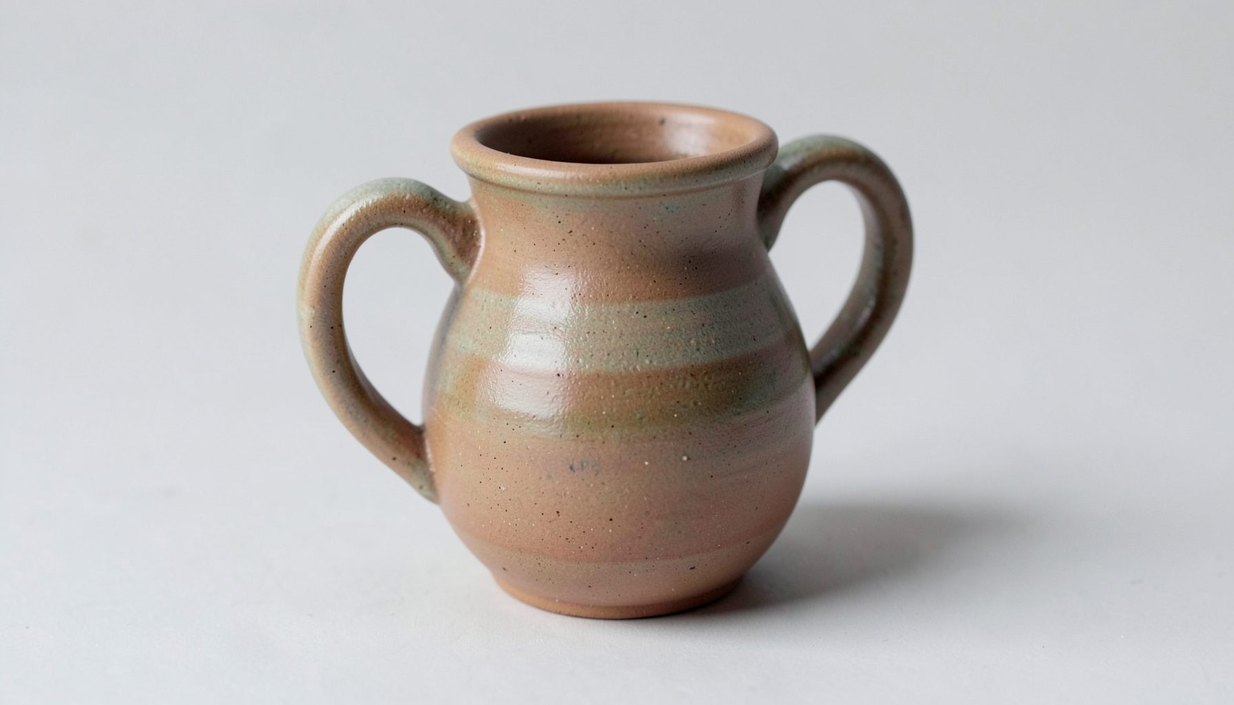 A small hand-built clay pitcher with a hollow handle, glazed in earthy muted tones