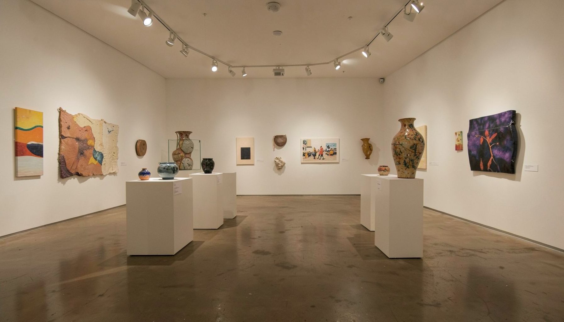 A community arts center gallery with track lighting and ceramic works on pedestals
