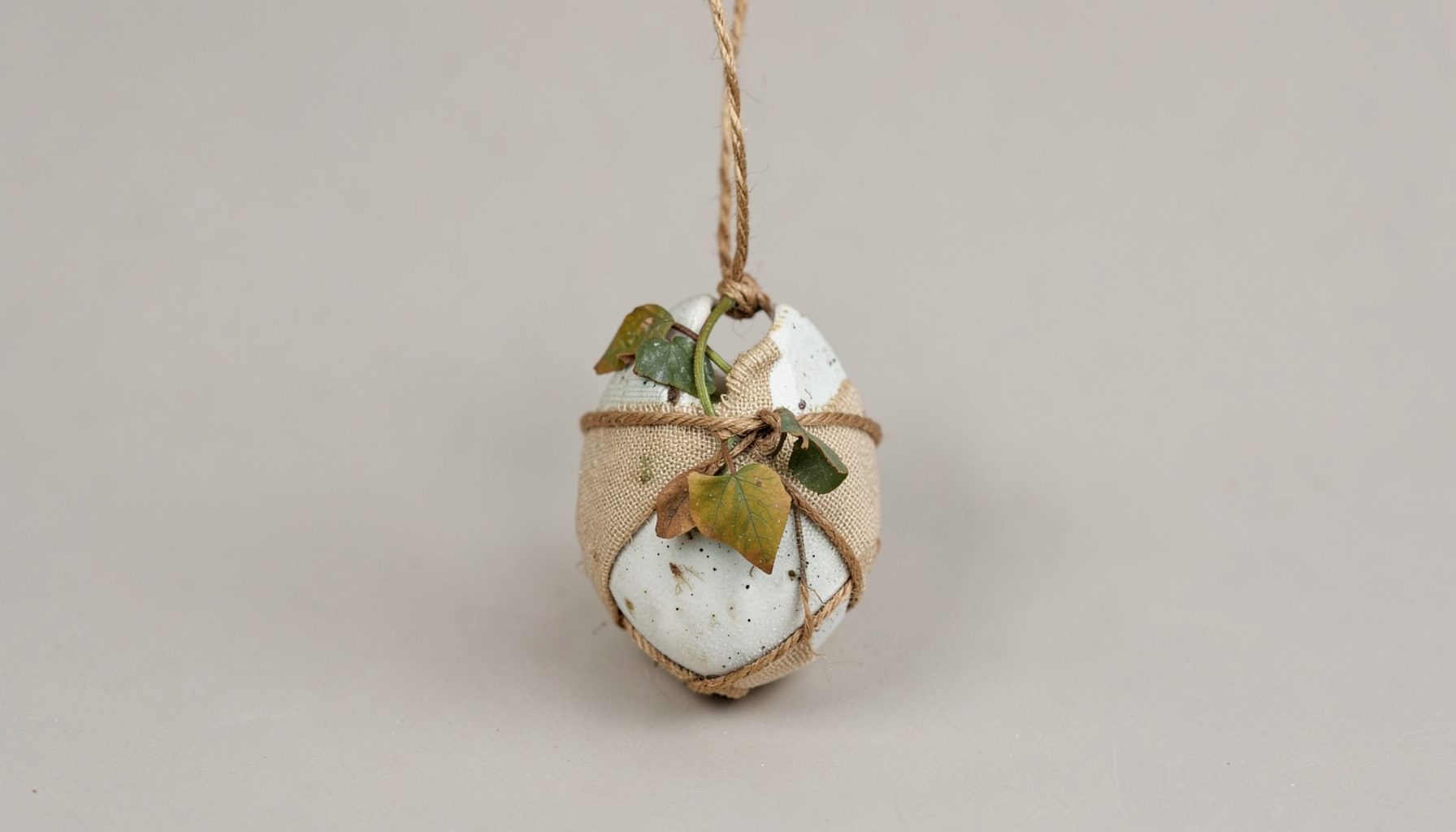 A wire-wrapped ceramic pendant with dried Virginia creeper vine wrapped in waxed linen, hanging against a neutral background
