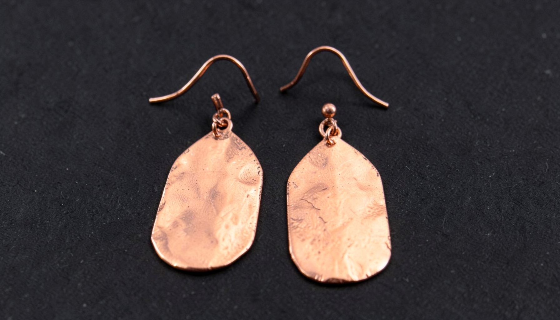 Copper paddle earrings with a warm metallic sheen, suspended from hammered copper earwires on a dark surface