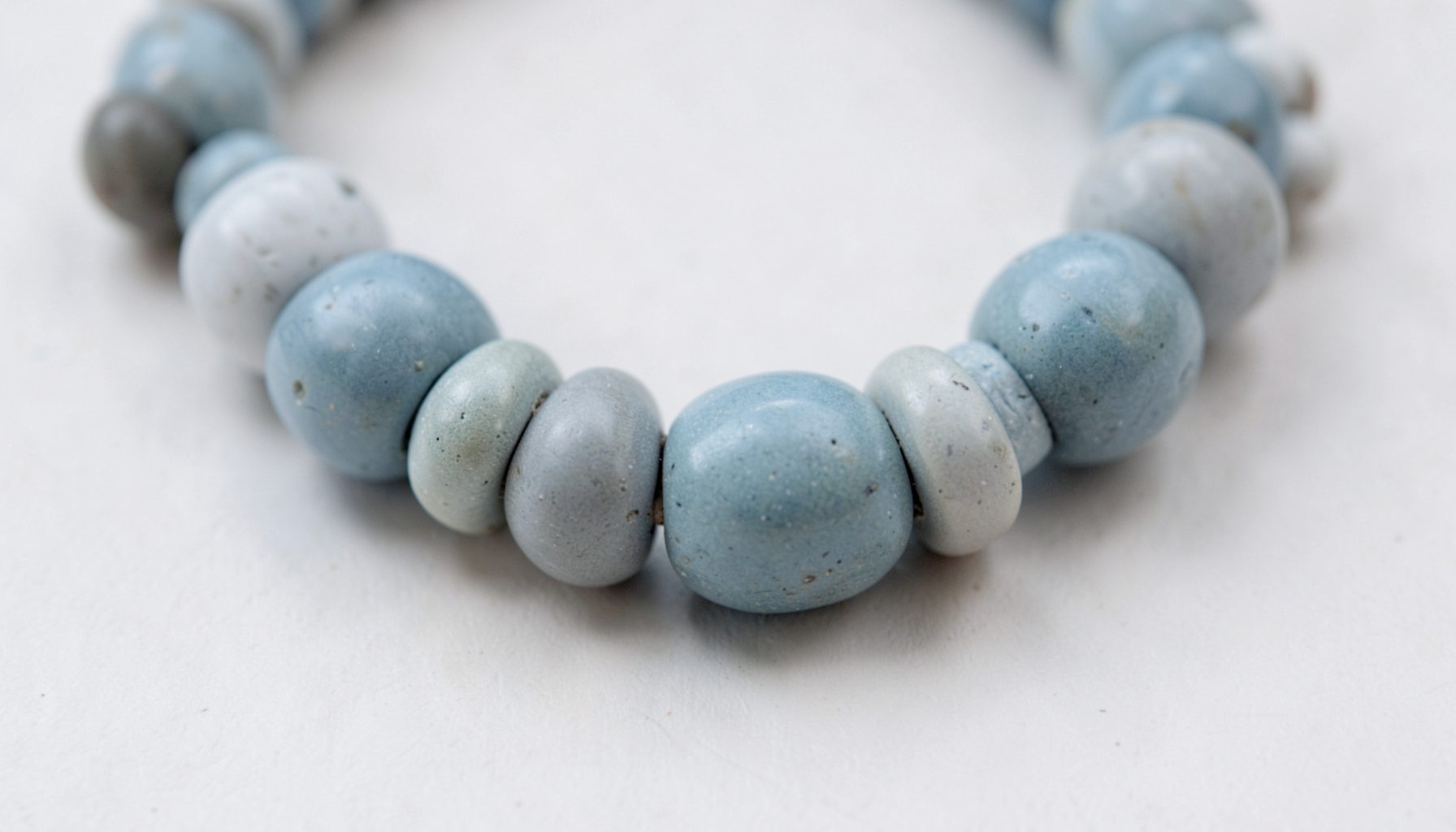 A close-up of a Blue Grey Gardens necklace — rounded stoneware beads in soft slate-blue and dove-grey, interspersed with Greek porcelain spacers