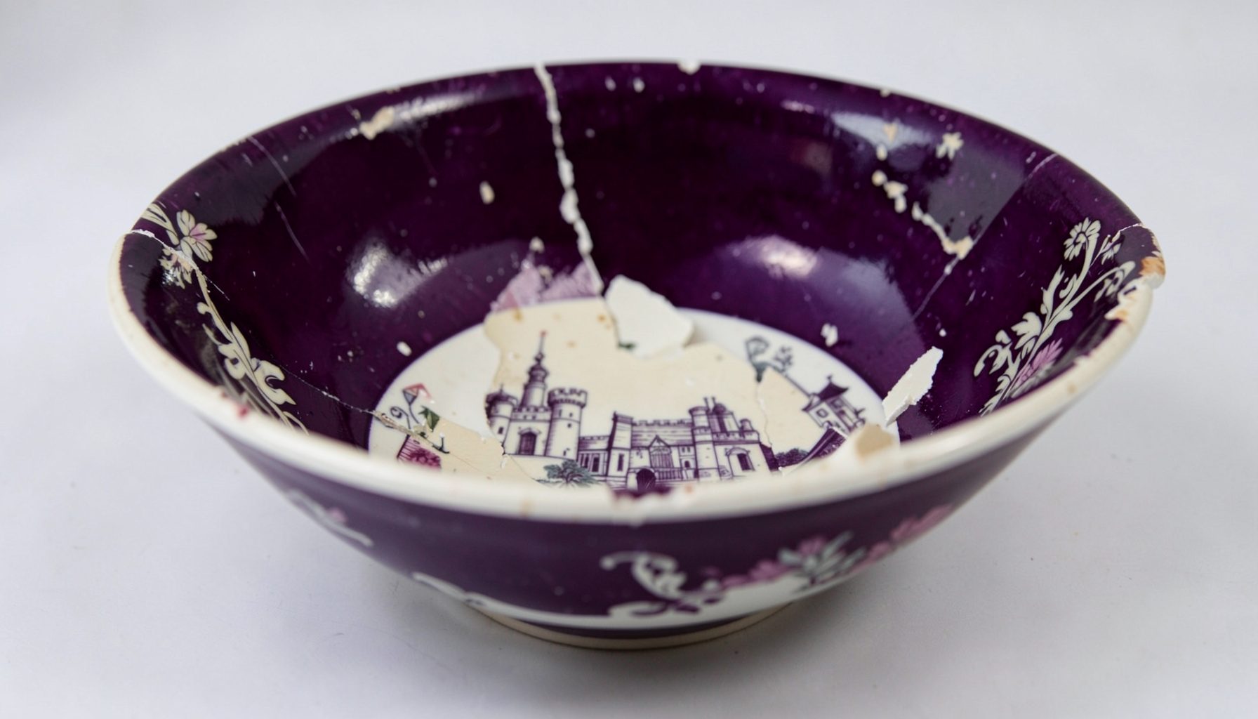 Broken shards of an antique English transferware bowl in deep aubergine and cream, with castle motifs visible on the curved fragments