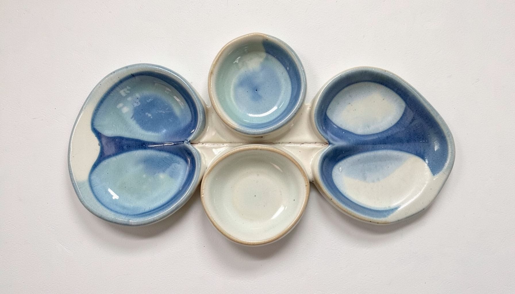 A ceramic wall piece titled Pentaphilia with five organic lobes, glazed in layered blues and soft ivory, mounted for exhibition display